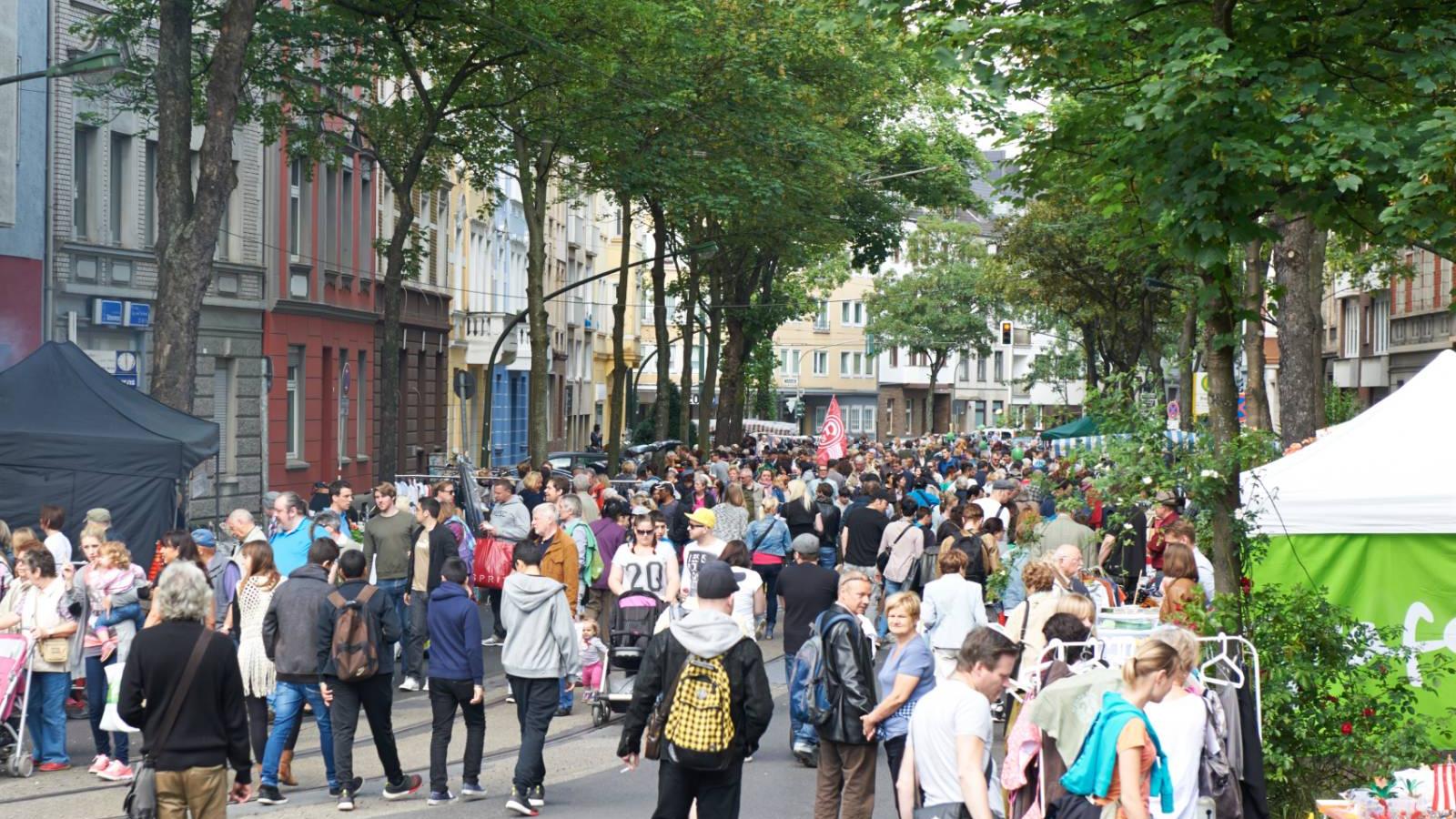Die Flurstraße beim Straßenfest, dicht gefüllt mit Menschen zwischen Altbauten, Bäumen und Ständen.